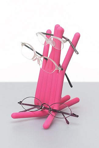 Pink glasses stand holding two pairs of eyeglasses, with another pair resting at the base.