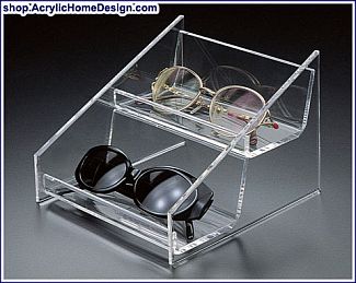 Acrylic two-tier eyeglass holder displaying two pairs of glasses. Text reads &quot;shop:AcrylicHomeDesign.com&quot;.