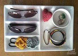 Tray with sunglasses, crocheted flowers, hair ties, bracelets, rings, a heart, and &#039;Island Closed Drawers&#039; text.