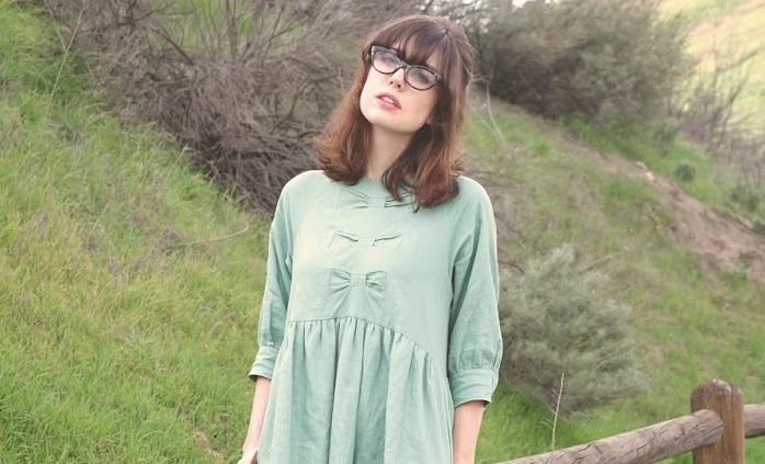 Woman wearing a light green dress with bow detailing below the neckline.