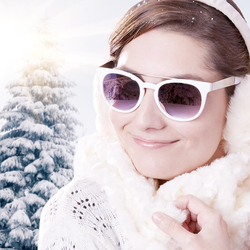 Woman wearing white-framed sunglasses and earmuffs in a snowy setting.