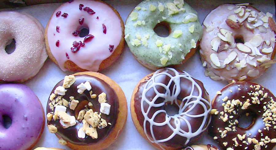 Assorted glazed donuts with various toppings including nuts, dried cranberries, marshmallows, and icing.