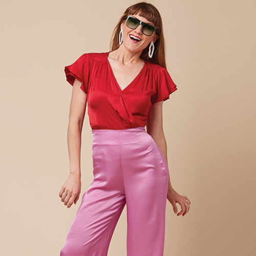 Woman wearing a red V-neck blouse with short sleeves and high-waisted, wide-leg pink satin pants.