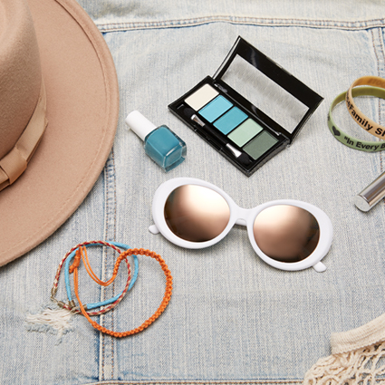 Wide-brimmed hat, blue nail polish, green and blue eyeshadow palette, white sunglasses, and orange bracelet.