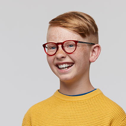 Child wearing stylish red-rimmed eyeglasses and a yellow textured sweater, smiling.