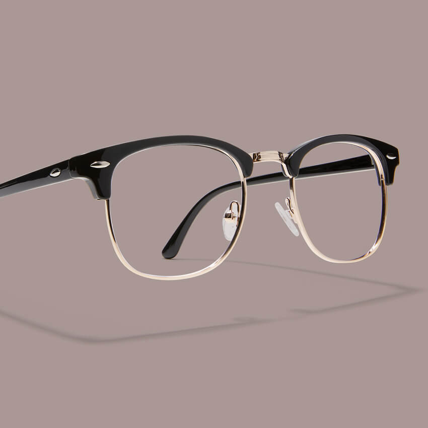 Clubmaster-style eyeglasses with black upper frame and gold lower rims and bridge on a light brown background.