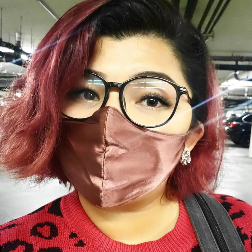 Person wearing a satin face mask, glasses, and a red sweater.