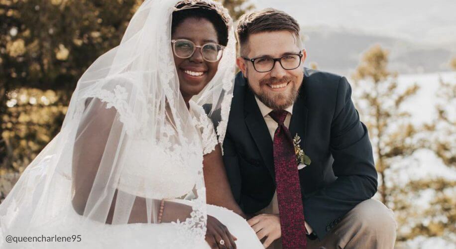 Bride in lace dress and veil, groom in suit with red tie, smiling together. @queencharlene95.