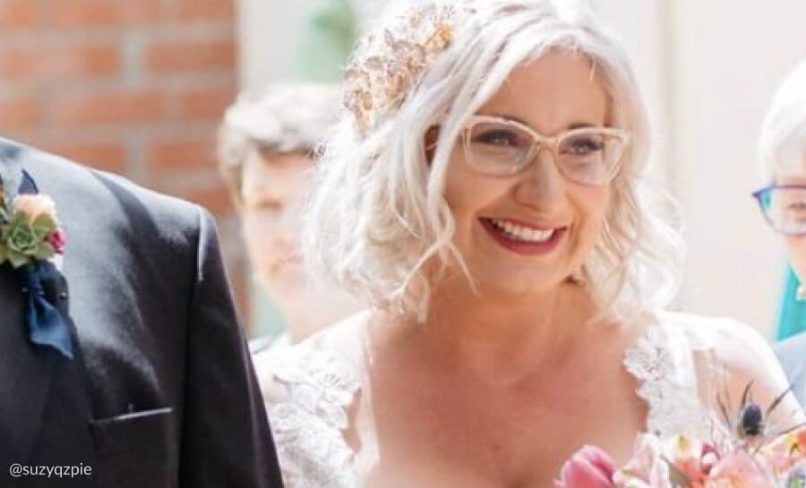 Smiling person with white hair wearing glasses, a lace dress, and a floral headpiece.