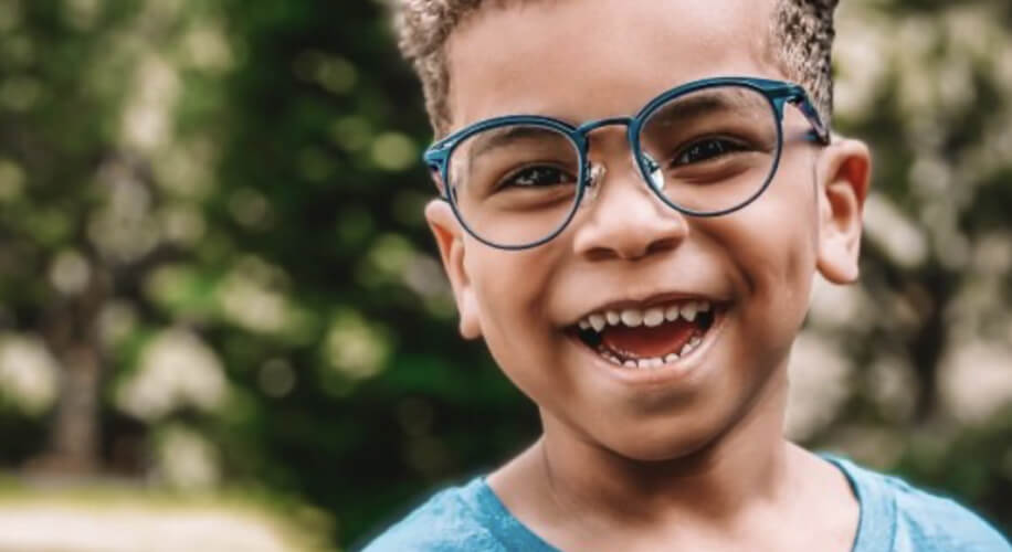 Child wearing blue glasses with a big smile.