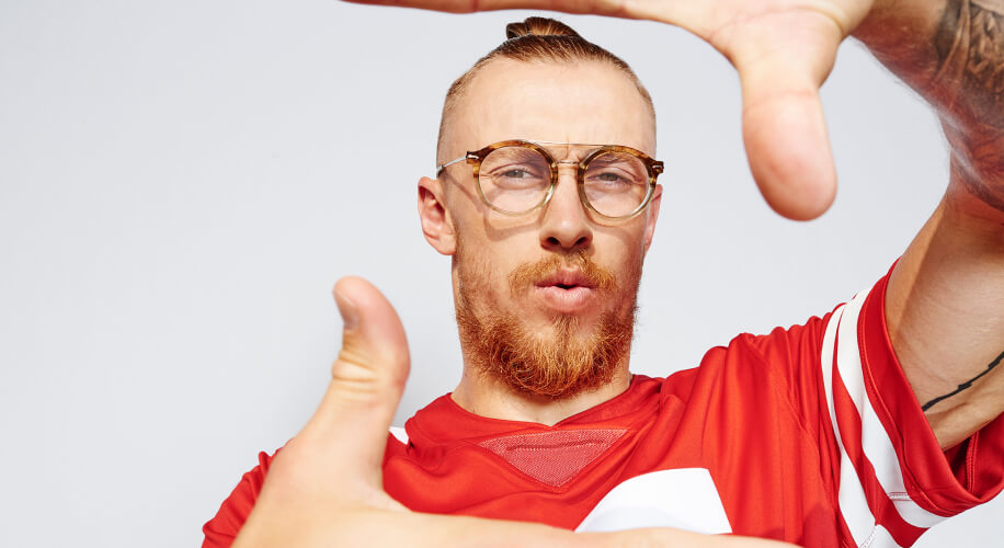 Man wearing glasses and a red sports jersey with white stripes, framing his face with his hands.