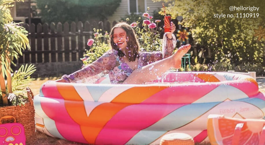 Person joyfully splashing in a colorful inflatable pool (@hellorigby style no. 1110919) with beverage in hand.