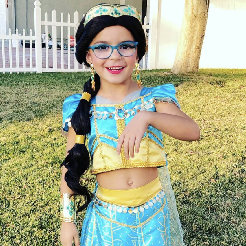 Child in a blue and gold princess costume with a long, dark braided wig and blue glasses.