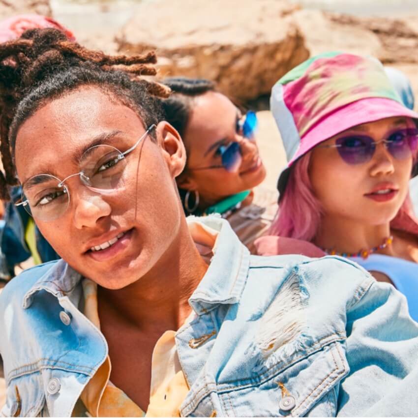 Three individuals wearing stylish sunglasses and casual outfits, enjoying a sunny day at the beach.