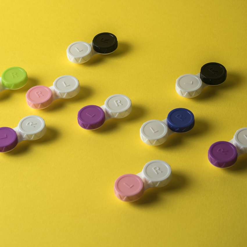 Colorful contact lens cases with "L" and "R" embossed on white caps against a yellow background.