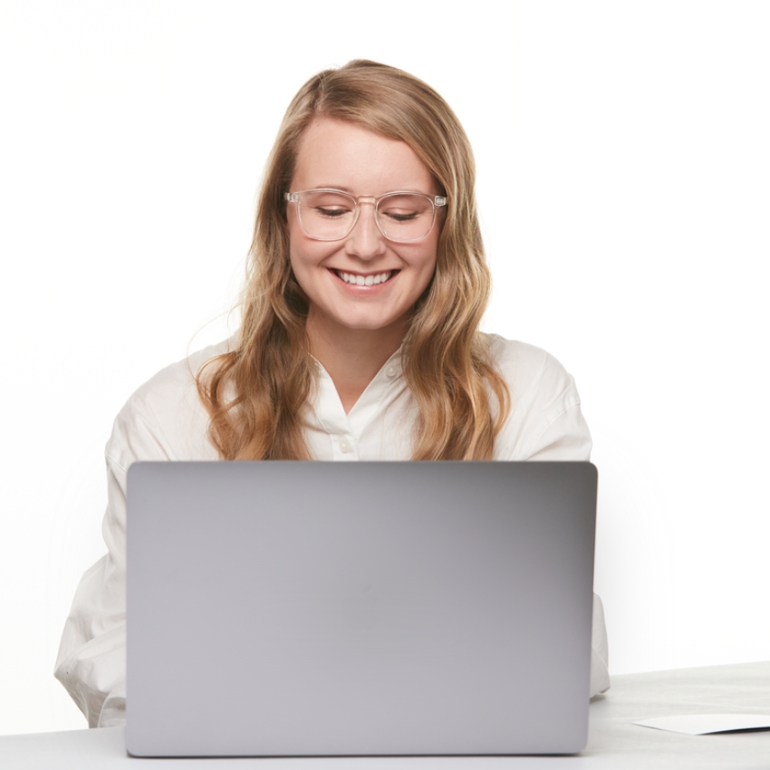 Person smiling at a laptop in a bright environment.