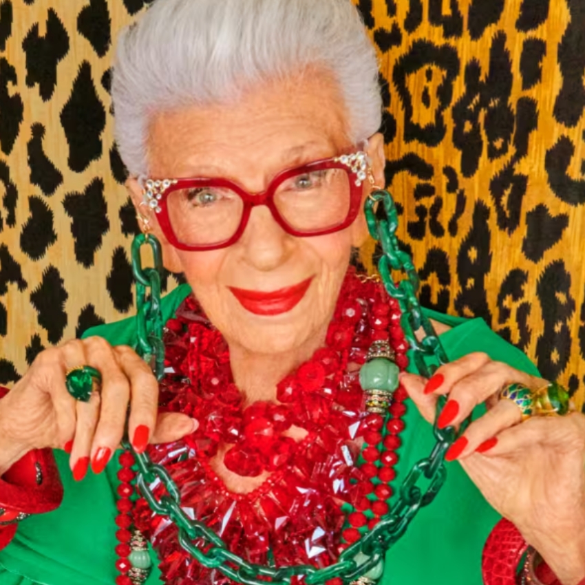 Woman wearing red glasses, a mix of chunky red and green necklaces, coordinating earrings, and green clothing.