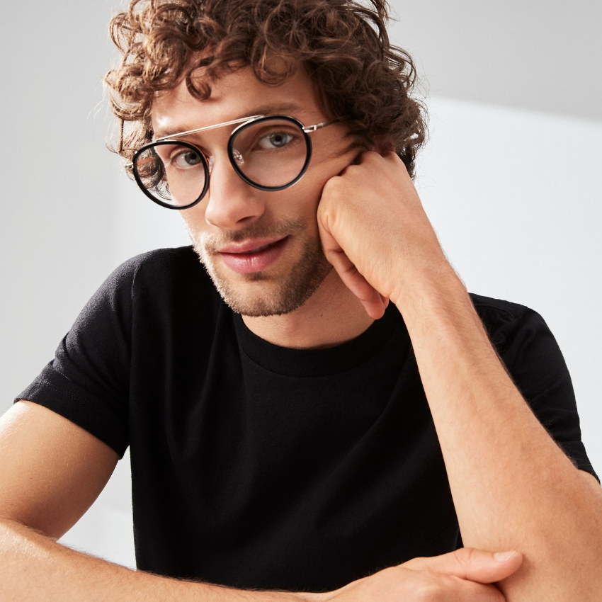 Round glasses with a silver bridge and black rims worn by a person in a black shirt.