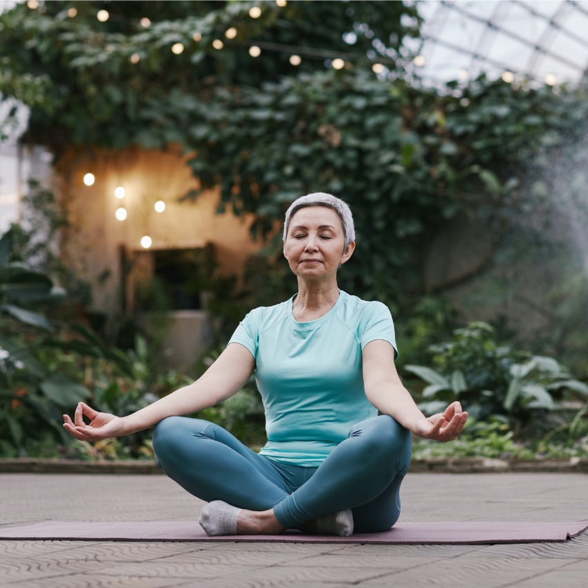 Person wearing teal activewear, sitting cross-legged on a yoga mat with hands on knees, meditating.