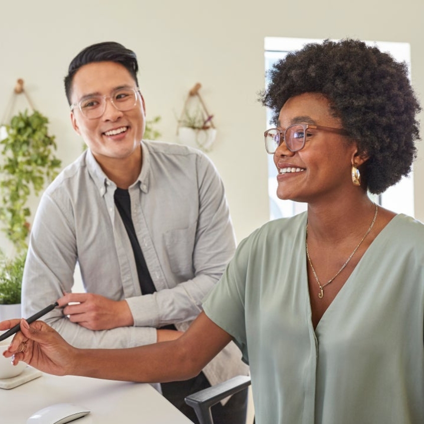 Two people wearing glasses, working together and smiling, one holding a stylus pen.