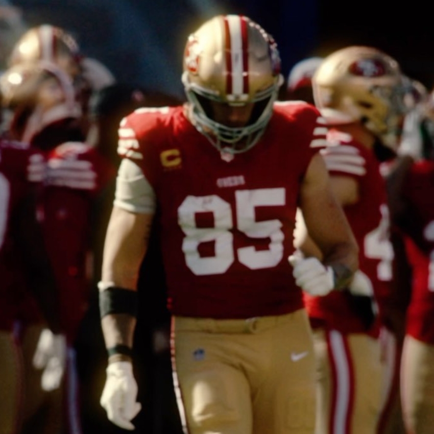 Football player wearing red jersey with number 85 and gold pants, heading onto the field.