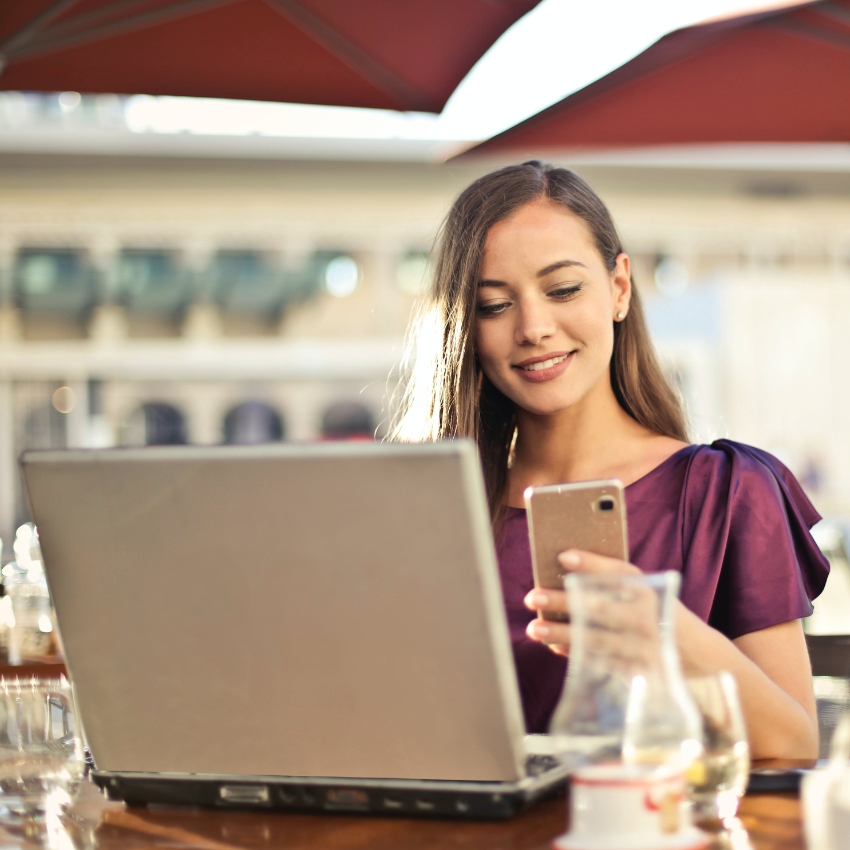 Woman using a laptop and smartphone at an outdoor café.