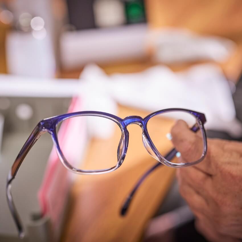 Hand holding blue and clear eyeglasses.