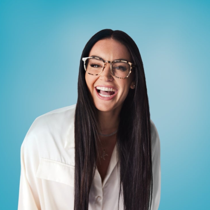 Woman with long dark hair wearing oversized tortoiseshell glasses, and a white shirt, smiling.