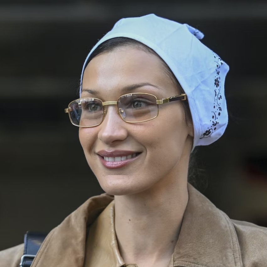 Woman wearing gold-rimmed glasses and a light blue headscarf with black detailing.