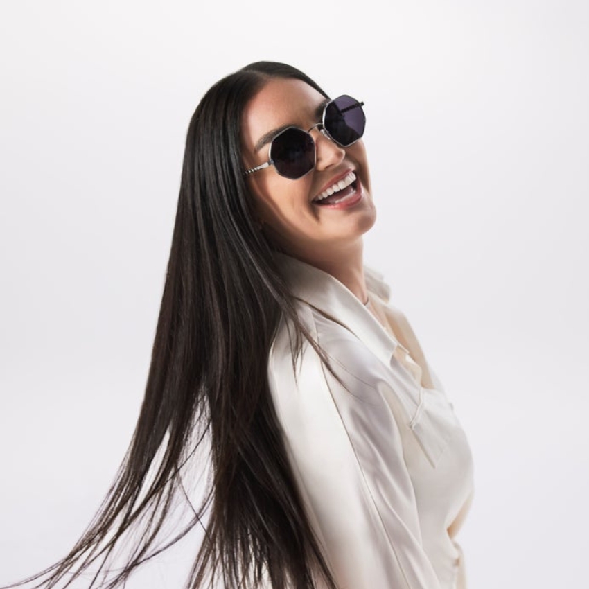 Woman wearing round, dark sunglasses with metallic frames, smiling with long, straight hair.