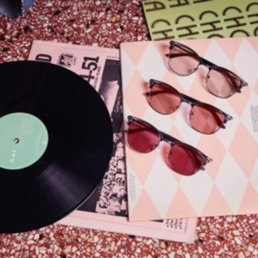 Three pairs of stylish sunglasses with pink tinted lenses next to a vinyl record and a magazine.