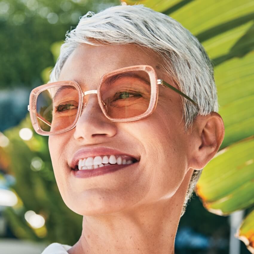 Woman wearing oversized, square, translucent pink sunglasses with amber lenses, smiling brightly.