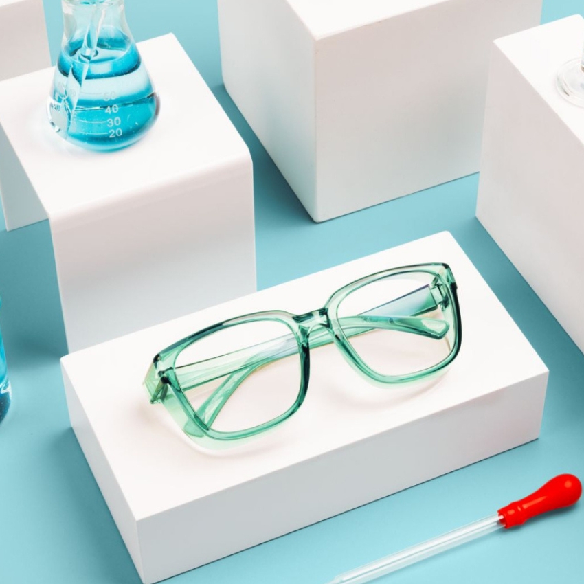 Green rectangular eyeglasses with clear lenses displayed on a white pedestal against a blue background.