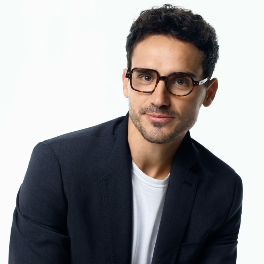 Man wearing tortoiseshell eyeglasses with a white inner shirt and dark blazer.