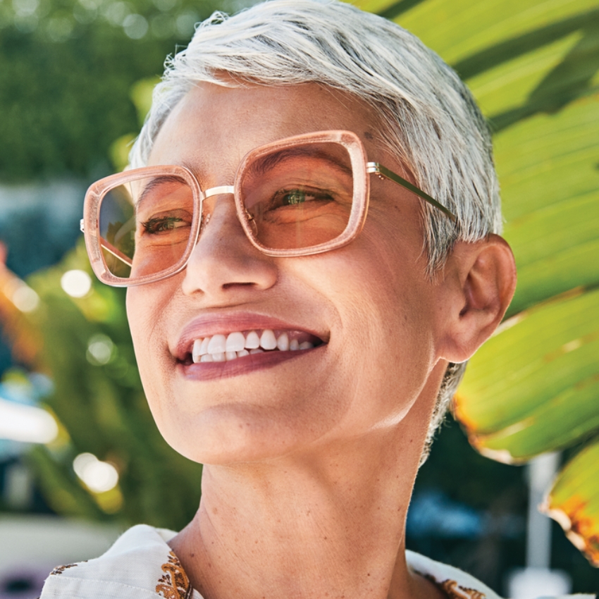 Woman wearing oversized, square, pink-tinted sunglasses with a metallic gold frame.