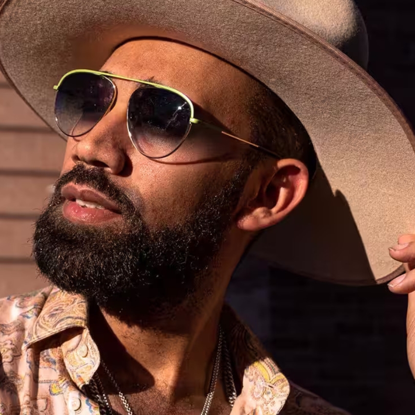 Man wearing aviator sunglasses and a wide-brimmed hat, tilting his head to the side.