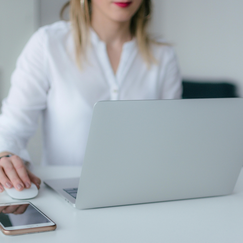 Woman using a silver laptop with a smartphone on the table.