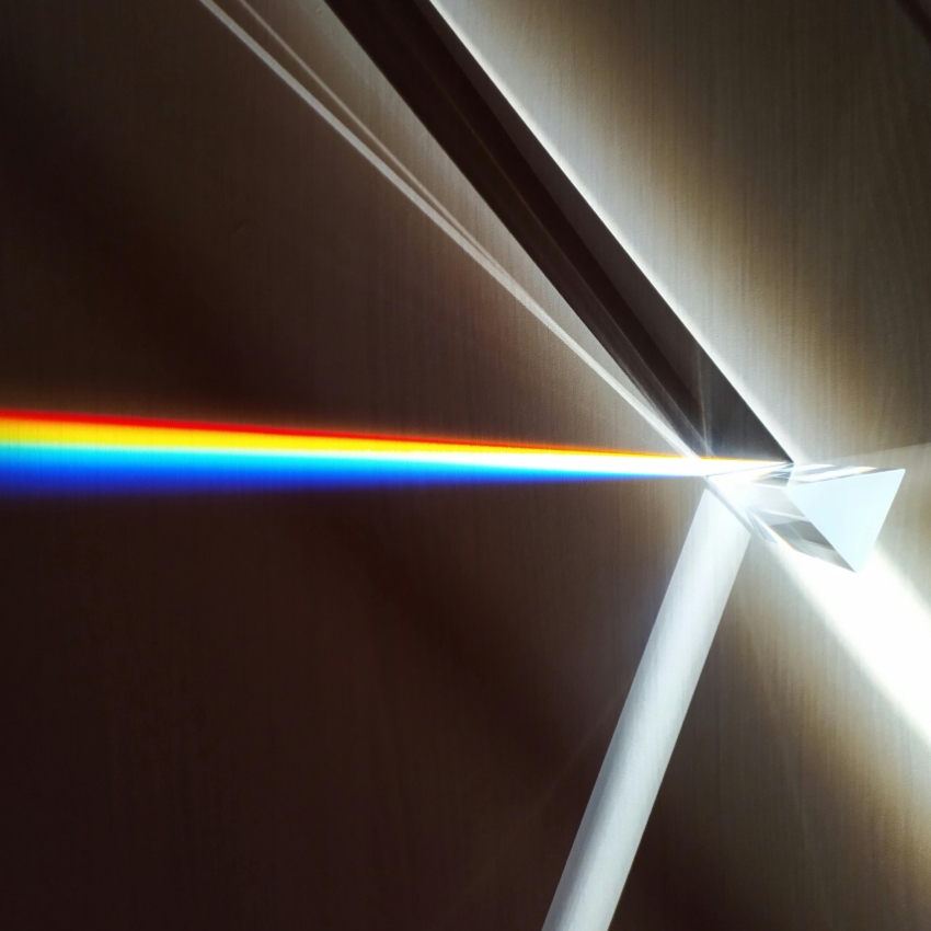 Glass prism refracting a white light beam into a vibrant spectrum of colors against a dark background.