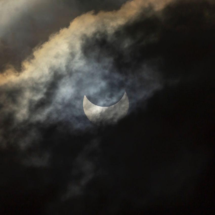 Crescent moon partially obscured by dark clouds in the night sky.