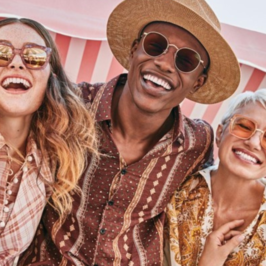 Three people wearing vintage-style sunglasses and patterned shirts smile joyfully.