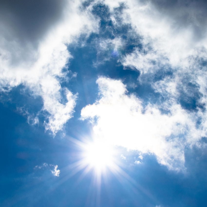 Bright sun shining through clouds in a blue sky.