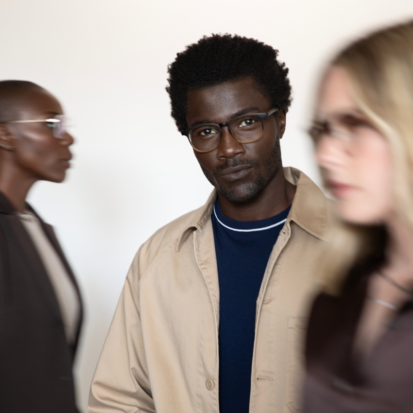 Man wears rectangular-shaped, dark-framed eyeglasses with a beige jacket and navy shirt.