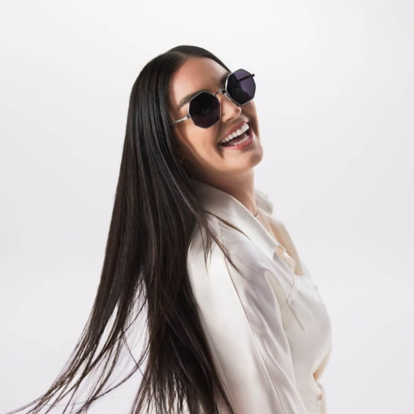 Woman wearing black geometric sunglasses and a white blouse, with long, shiny, straight hair.