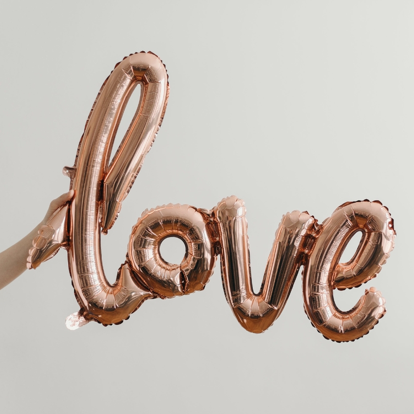 Rose gold balloon letters spelling "love" held by a hand.