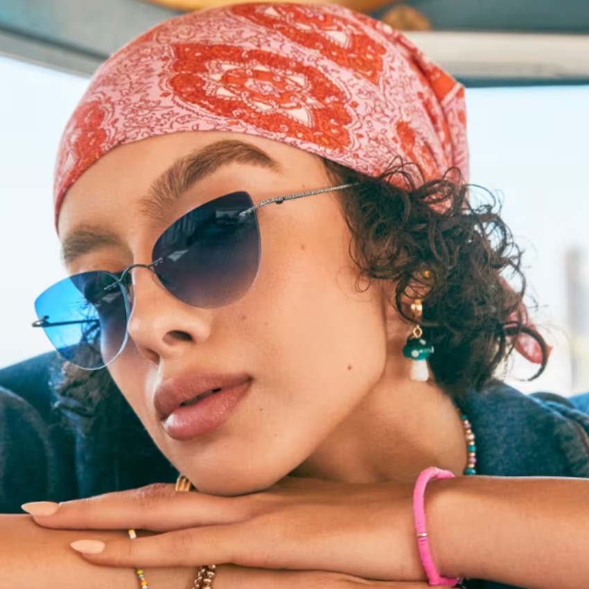 Woman wearing blue gradient sunglasses, a red patterned headscarf, teal earrings, and a pink bracelet.