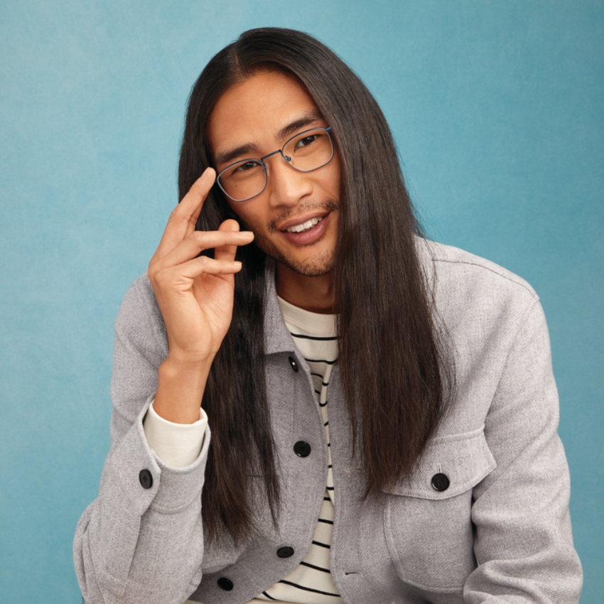 Person wearing blue-rimmed eyeglasses, a light grey jacket with black buttons, and a striped shirt.