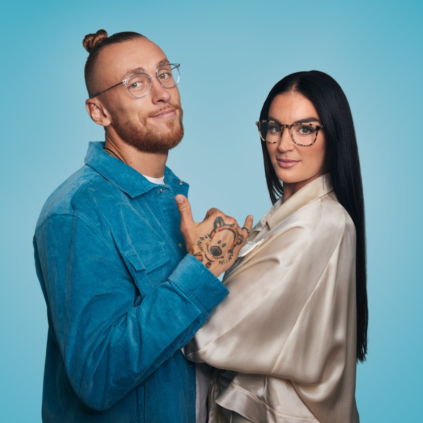 Man wearing circular eyeglasses, blue denim jacket. Woman wearing tortoiseshell eyeglasses, satin blouse.