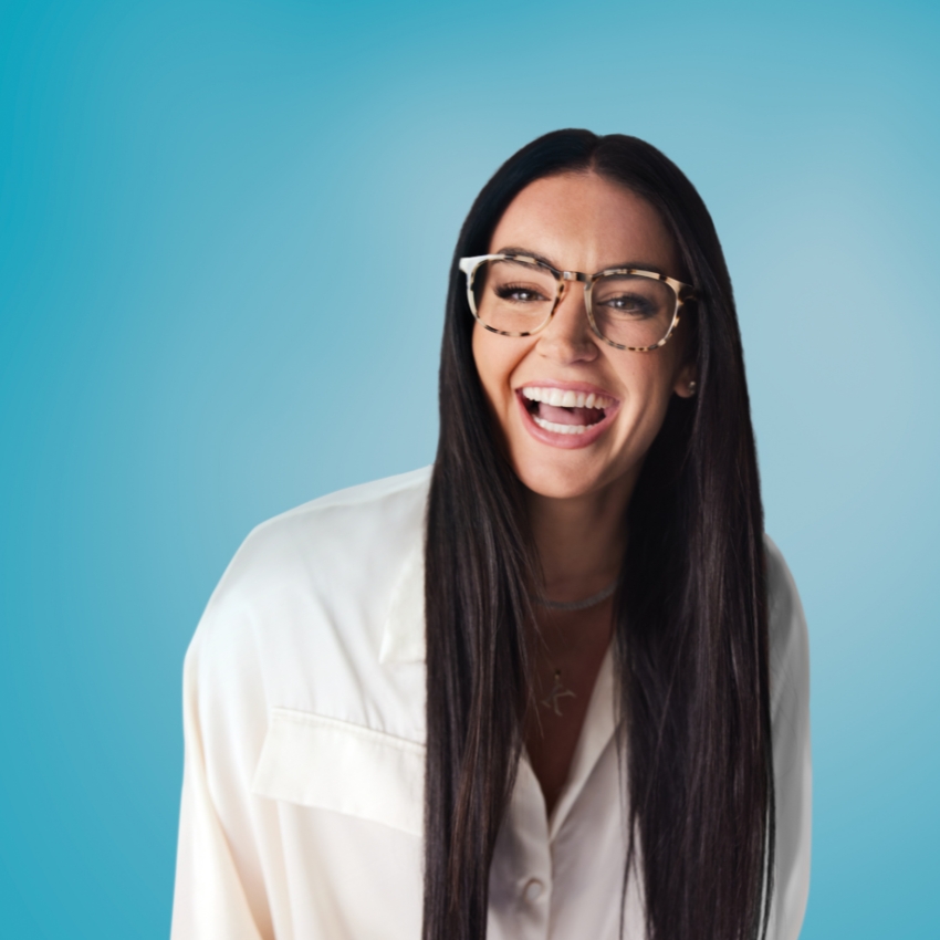 Woman wearing tortoiseshell eyeglasses with a wide smile, dressed in a white button-down shirt.