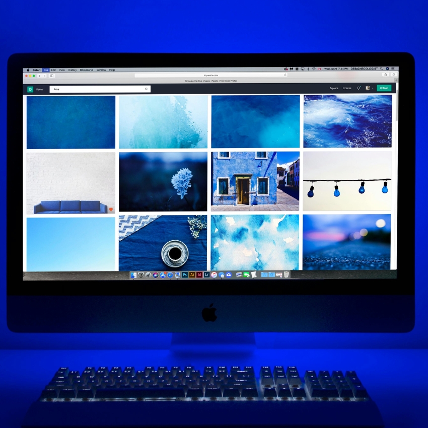 Apple iMac displaying a grid of blue-themed photos. A keyboard is placed below the screen.