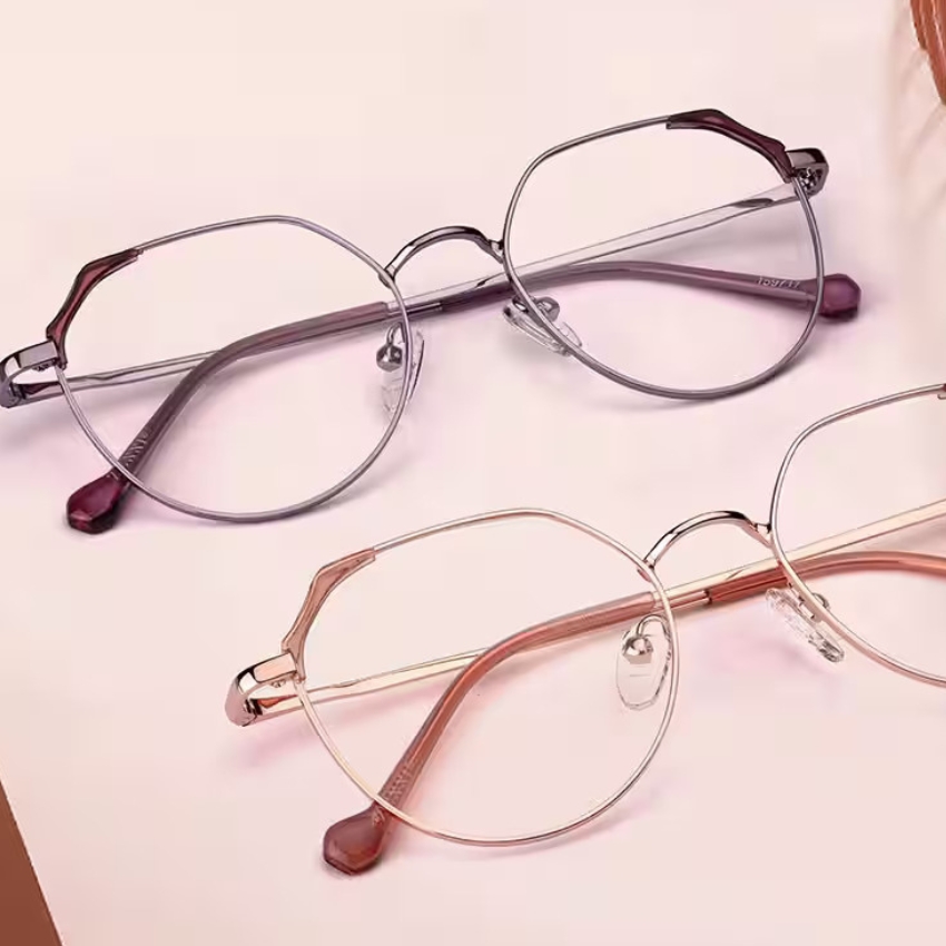 Two pairs of eyeglasses with round frames, one in silver and the other in gold, lying on a light surface.